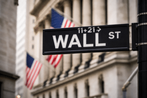 Wall Street street sign in New York with American flags and the New York Stock Exchange building in the background.